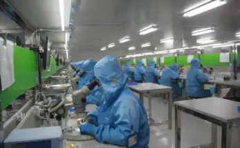 scientists in blue suits looking in microscopes in a laboratory