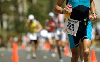 Marathon runner wearing blue one piece bathing suit holding a bottle of water with three runners behind him on the street