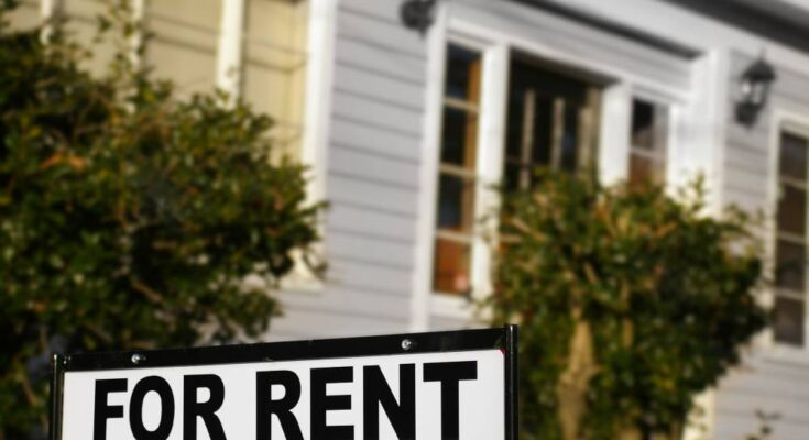 A sign with the words "For Rent" outside in the front yard of a home.