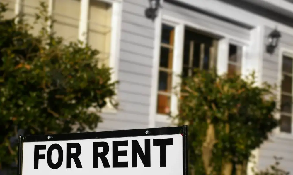 A sign with the words "For Rent" outside in the front yard of a home.