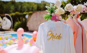 Pink bridesmaid robes hanging behind a white robe labeled "bride", and a pool with flamingo floats in the background.