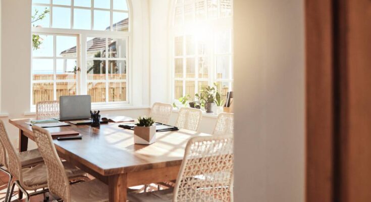 A sunroom with white walls, arched windows, and a wood dining room table with eight woven dining room chairs.