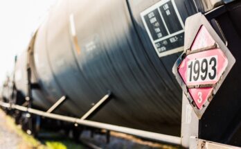 black chemical transportation containers on a locomotive train with a red sign that reads "1993" to label the chemicals