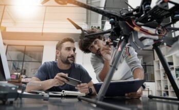 Two engineers in their large office working together as they inspect the mechanics of a drone that sits on their desk.