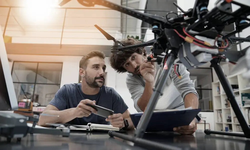 Two engineers in their large office working together as they inspect the mechanics of a drone that sits on their desk.
