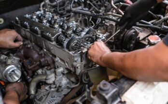 Two mechanics working on various parts of a diesel engine. One is using a tool to perform maintenance on the engine.