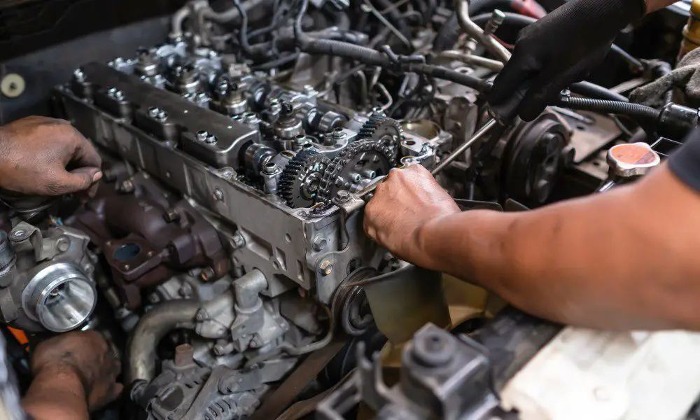 Two mechanics working on various parts of a diesel engine. One is using a tool to perform maintenance on the engine.