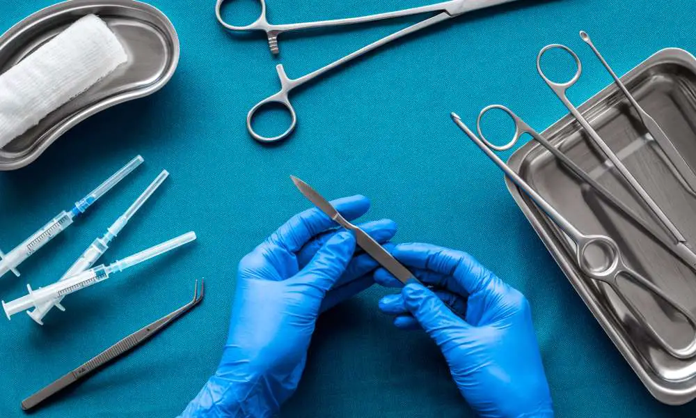 Doctor's hands holding a scalpel with surgical tools arranged on a blue background as he prepares for surgery.