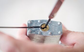 The bottom of a silver lock with a gold keyhole getting picked with a tension wrench and a pick.