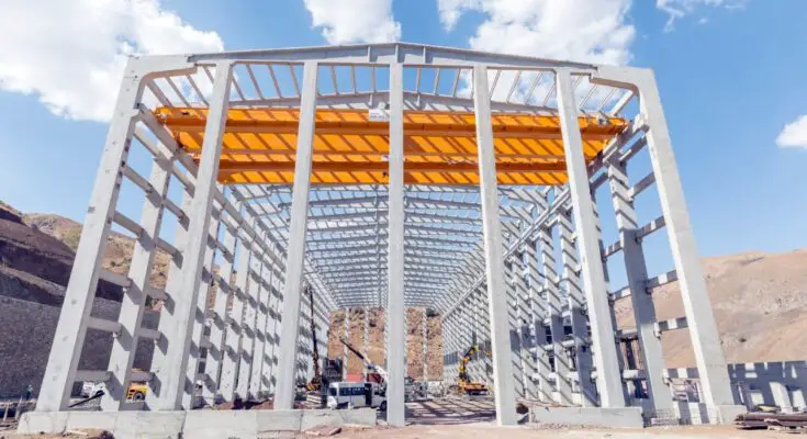 A large metal structure in the process of being built. There are various construction vehicles and materials around it.