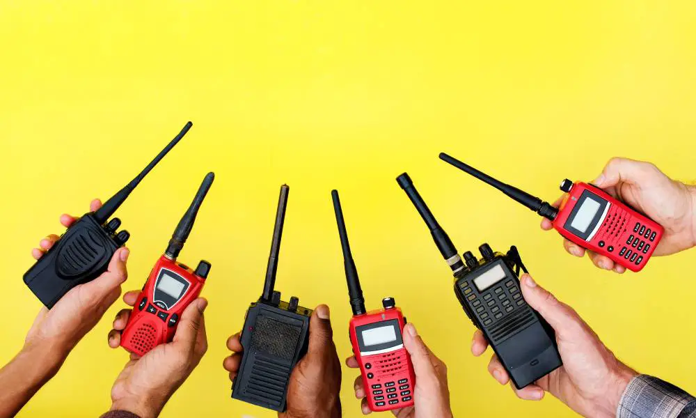 Six hands holding up red and black two-way radios in an alternating color pattern in front of a yellow background.