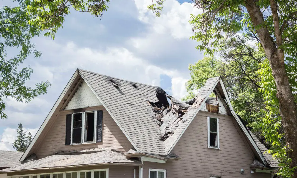 A house surrounded by trees and clouds is the victim to fire damage. The roof is caved in at parts because of the damage.