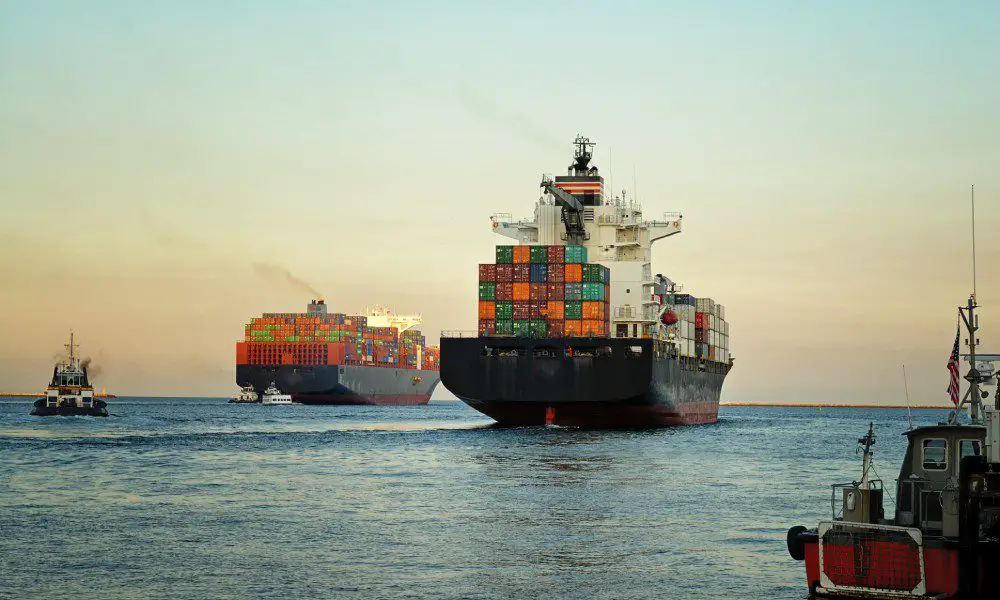 A large container ship at sea with stacks of cargo containers. There's a second container ship in the background.