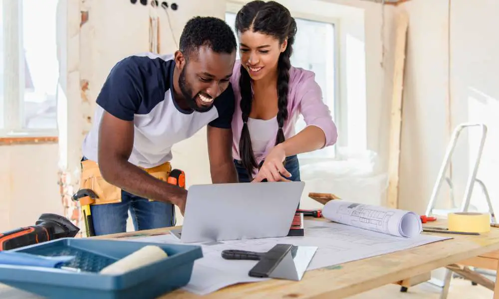 Two young homeowners preparing for home renovations by exploring different design plans on their shared laptop.