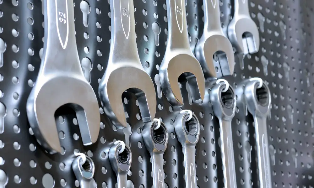 A collection of manual wrenches and spanners placed in ascending order of size on a black pegboard.