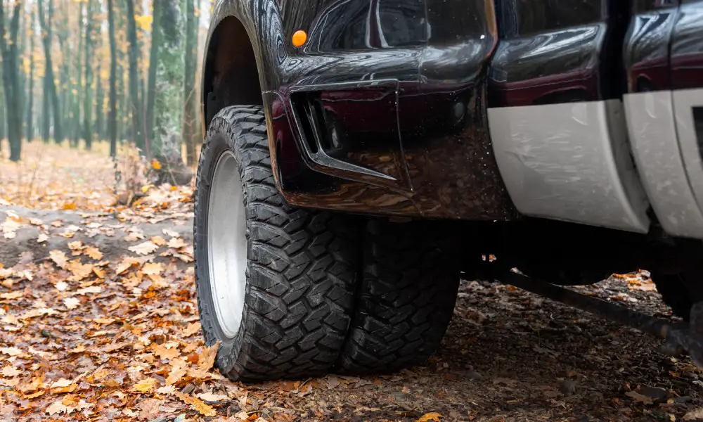 The large front driver's side wheel on an extra-large pickup truck is visible. The setting is an autumnal scene.