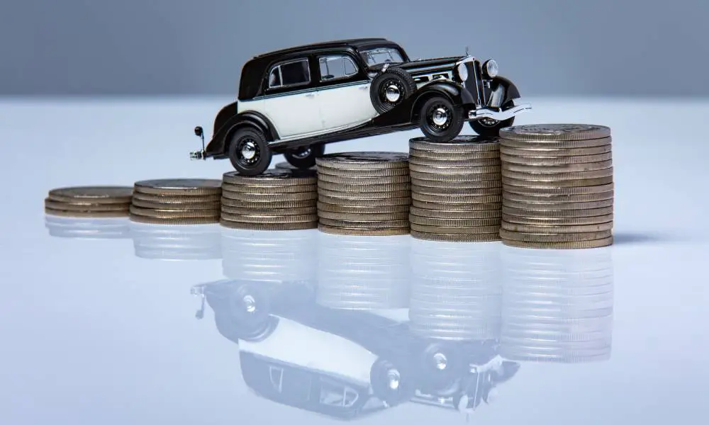 A black-and-white classic car stands on top of a stack of coins, and its reflection appears underneath the table.