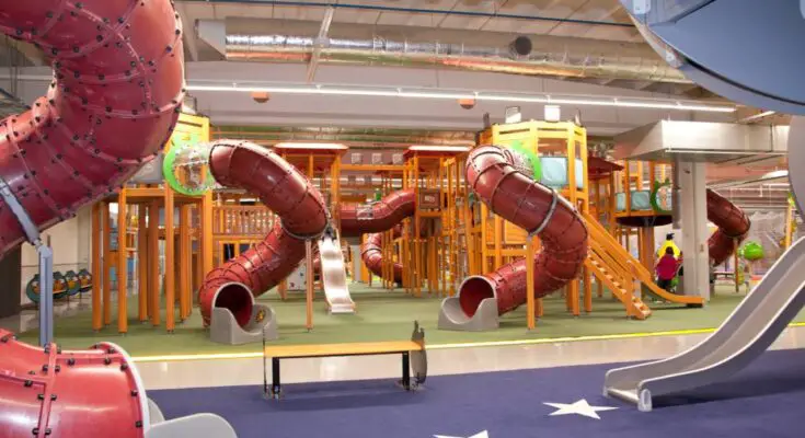 An indoor playground with numerous red metal slides with a spiral curvature and dark-blue rubber surface for flooring.