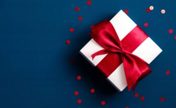 A white gift box tied with a red ribbon and red circular confetti on a dark blue background.