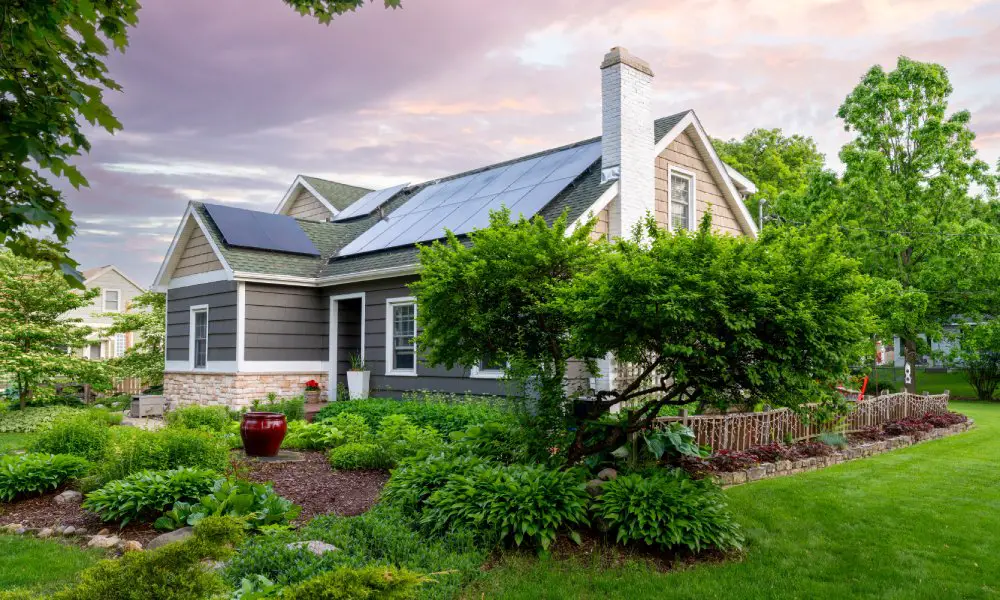 A beautiful East Coast-style residential home with roof-installed solar panels. The house is surrounded by lush landscaping.
