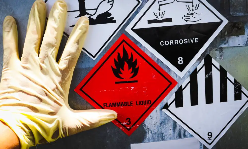 Close-up on a gloved hand touching a container that has warning stickers on it that say FLAMMABLE LIQUID and CORROSIVE.