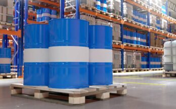 A warehouse with dozens of blue and white barrels and plastic containers placed on pallets and high metal shelves.