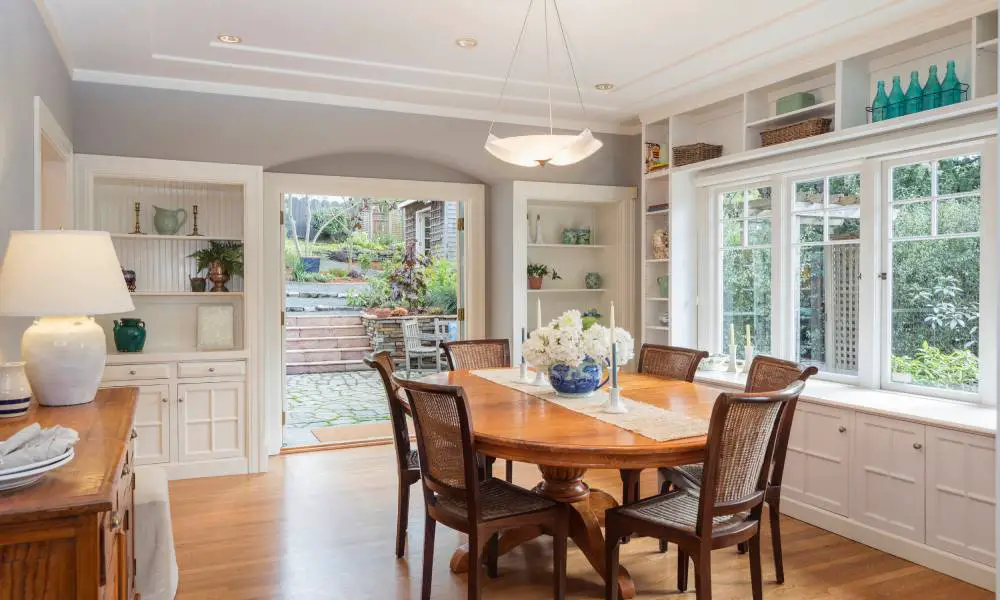 A traditional family dining room with shelving and hidden cabinets around the room. There's a bay window with a ledge.