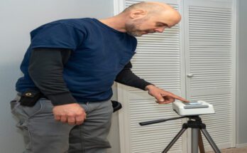 A man wearing a blue shirt and cargo pants sets up a radon test in a room. He is standing near a closet.