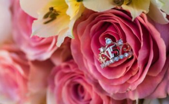 A silver ring shaped like a tiara with the number "15" at its center displayed in a bouquet of roses and lilies.