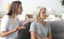 An annoyed young woman and her older mother on a couch. The daughter is gesturing toward her mother, who is turned away.