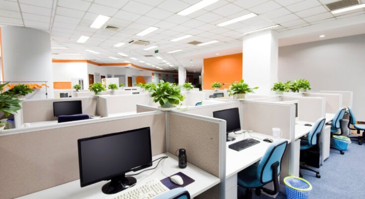 An office filled with cubicles that have low partitions. The device cords in each cubicle go through desk grommets.