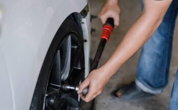 A close-up of a person in jeans and outdoor sandals carefully tightening the lug nuts on a car's wheel.