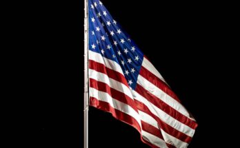 A tall flagpole proudly displaying a beautifully lit up American flag, soaring high in the night sky.