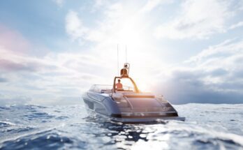 A man is driving a boat on an open body of water towards the sunset. The water has waves, and the sky has clouds.