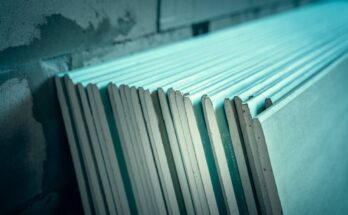A close-up of a stack of green moisture-resistant drywall sheets leaning up against a brick wall.
