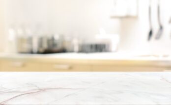 A close-up view shows a white, expensive-looking countertop that contains gray lines throughout. The background is blurry.