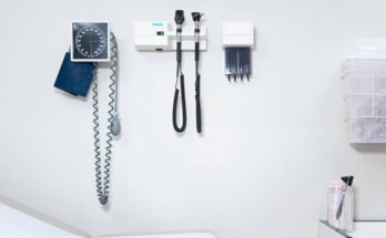 A blood pressure monitor and other equipment is mounted on a white wall in a clean doctor's office.