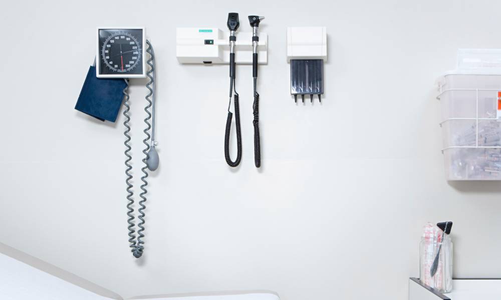 A blood pressure monitor and other equipment is mounted on a white wall in a clean doctor's office.