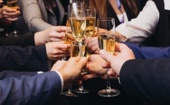 Multiple people in business attire hold filled champagne glasses together in a circle as they toast.