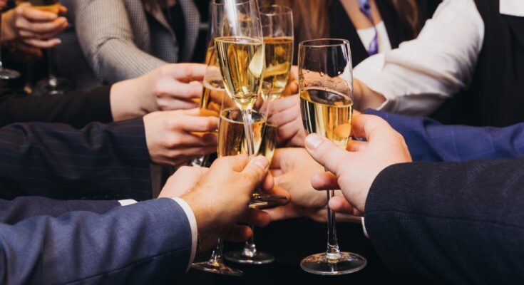 Multiple people in business attire hold filled champagne glasses together in a circle as they toast.
