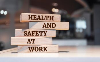 There are small wooden blocks on a desk, each reading a different word, creating the sentence, "HEALTH AND SAFETY AT WORK."