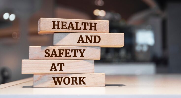 There are small wooden blocks on a desk, each reading a different word, creating the sentence, "HEALTH AND SAFETY AT WORK."
