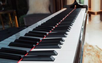 A close-up of the keys of an upright piano placed in the room of a home with a bench in front of it.
