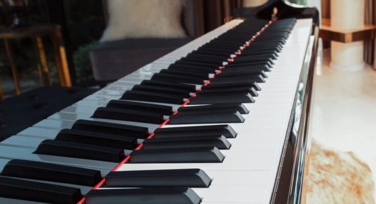 A close-up of the keys of an upright piano placed in the room of a home with a bench in front of it.