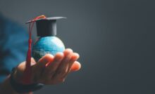 A close-up of a person's hand cupping a miniature version of the world globe with a graduation cap on it.