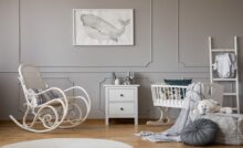 A baby nursery with a gray, neutral interior design, furnished with a bassinet, rocking chair, and toys.