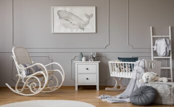 A baby nursery with a gray, neutral interior design, furnished with a bassinet, rocking chair, and toys.