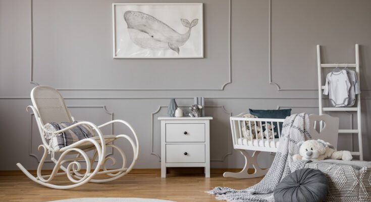 A baby nursery with a gray, neutral interior design, furnished with a bassinet, rocking chair, and toys.