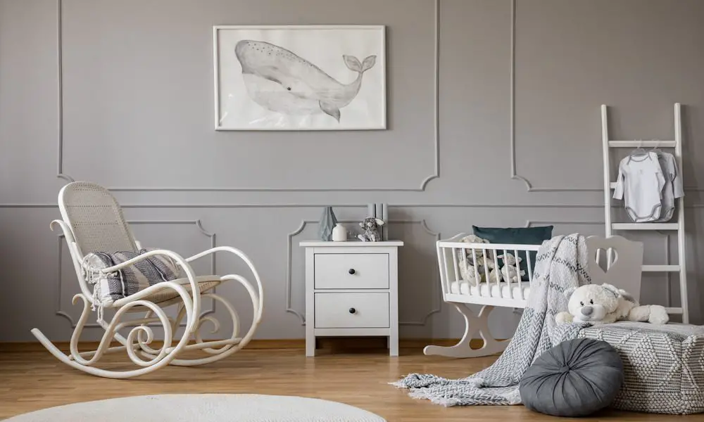 A baby nursery with a gray, neutral interior design, furnished with a bassinet, rocking chair, and toys.