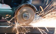 A close-up view shows a person using a handheld saw on a piece of metal. Sparks are flying around the saw.